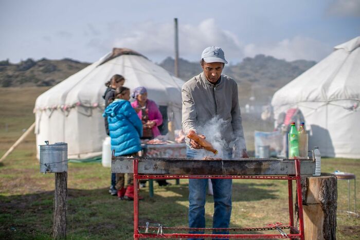 A man grilling food outside yurts, a scene that reminds Americans to be respectful when visiting other countries.