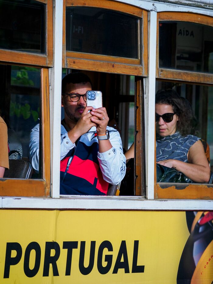 An American man taking a photo from a tram in Portugal, emphasizing the importance for Americans to be respectful travelers.