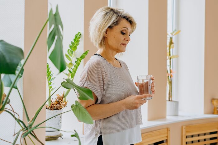 A woman holding a glass of water indoors, showing how pink taxes make being a woman more difficult.