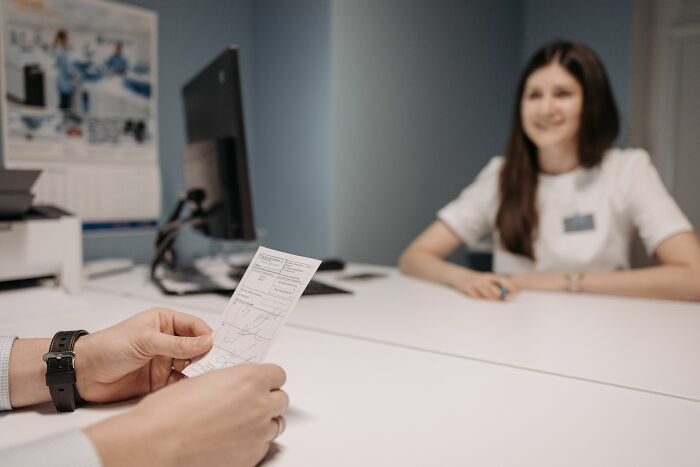 Pink taxes affecting women: A person's hands holding a document across a table from a smiling woman.
