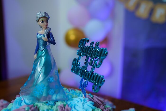 An Elsa figurine and Happy Birthday topper on a cake, symbolizing how pink taxes make being a woman more difficult.
