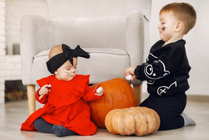 Two babies dressed in Halloween costumes next to pumpkins, illustrating how pink taxes make being a woman more difficult.