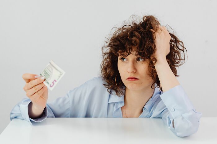 A woman looking frustrated while holding a 5 dollar bill, illustrating the financial burden of pink taxes.