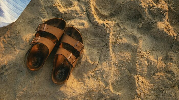 Brown sandals on sandy beach, symbolizing how pink taxes make being a woman more difficult.