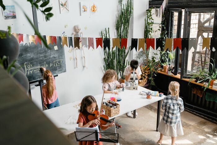 Children in a classroom, with one playing violin and another using a microscope. This image does not directly relate to pink taxes.