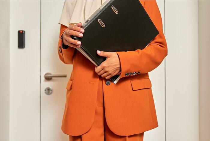 Woman in an orange suit holding a binder, illustrating pink taxes that make being a woman more difficult.