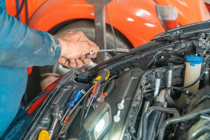 Mechanic working on a car engine, highlighting pink taxes making being a woman more difficult for car services.