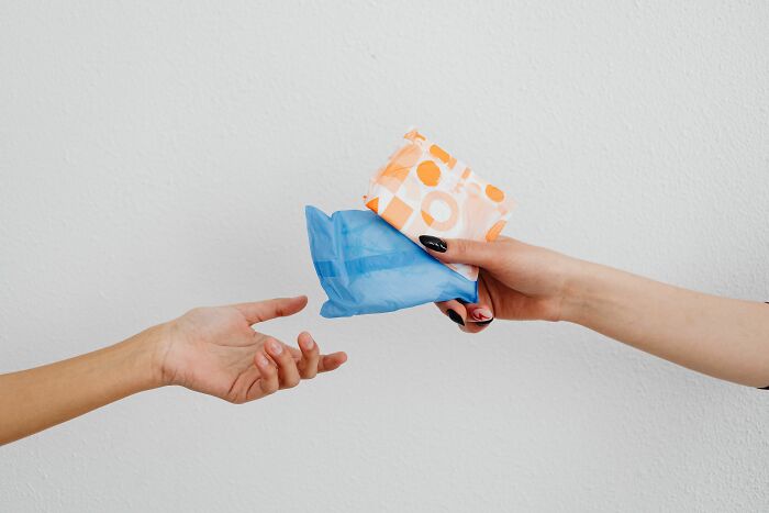 One hand giving menstrual pads to another, showing an example of pink taxes affecting women.