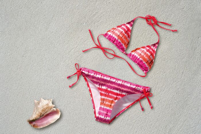 A pink tie-dye bikini on sand next to a seashell, symbolizing how pink taxes affect women's products.