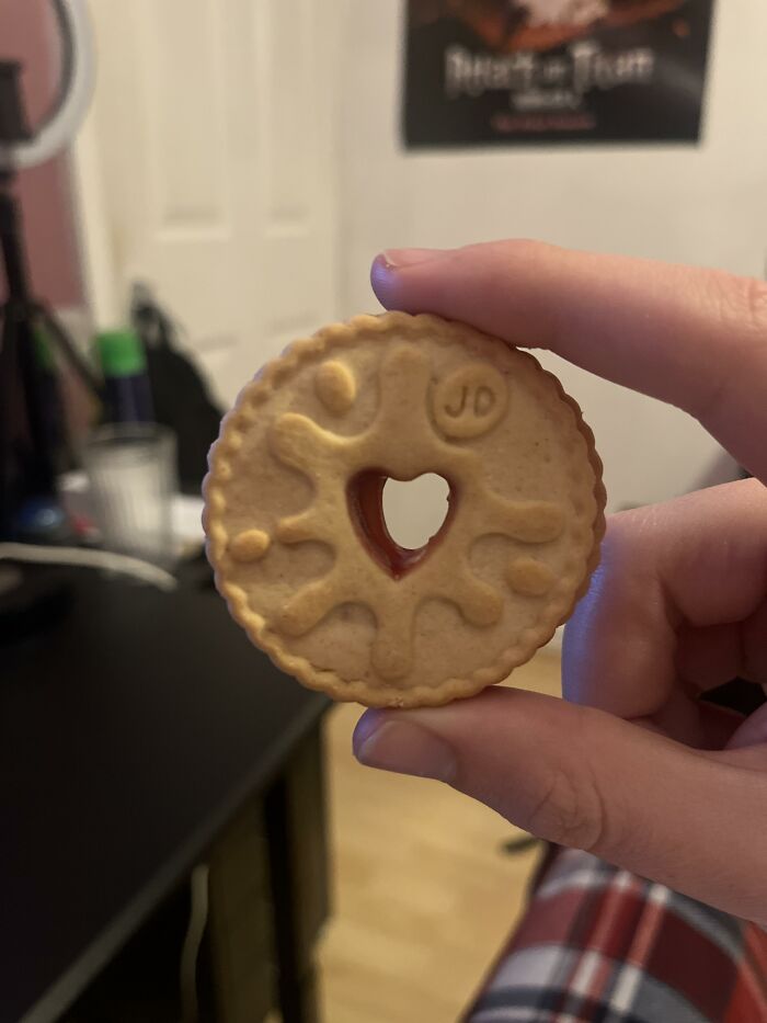 A hand holding a Jammie Dodger biscuit with a heart-shaped jam center, illustrating a fun aspect of British humor.