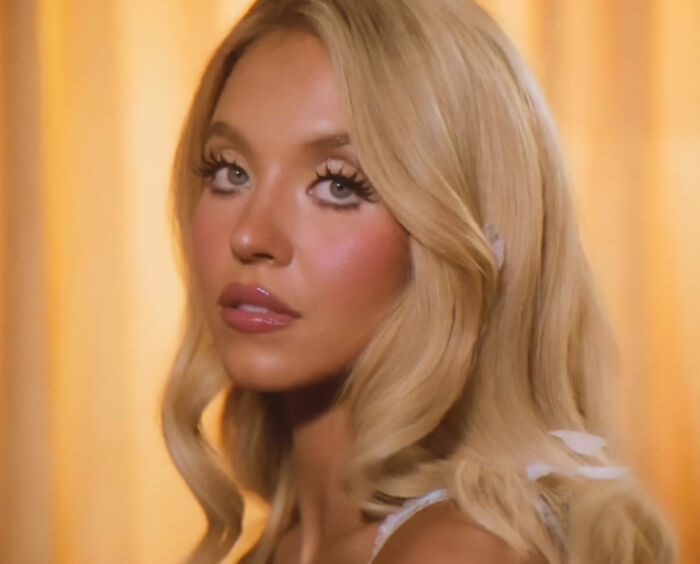 Close-up of Sydney Sweeney from SYRN lingerie video, with dramatic eye makeup and pink blush.