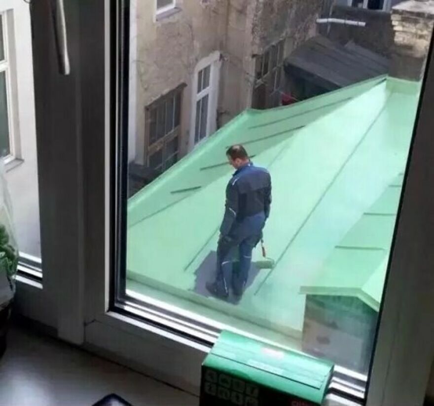 A man painting a rooftop in a funny and unfortunate way, standing on the green painted surface.