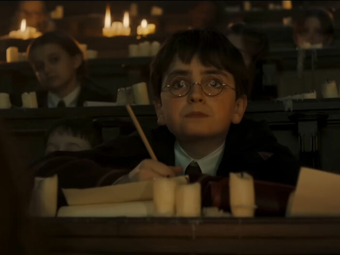 A young Harry Potter character in a classroom scene from the series, with candles illuminating the setting.