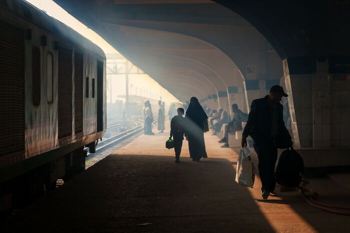 A woman and child walk on a sunlit platform by a train, capturing life's funniest coincidences in street photos.