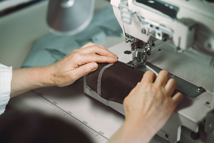 Hands guiding fabric under the needle of a sewing machine, unrelated to pet owners or vet bills.