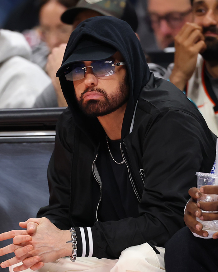 Eminem looking contemplative in a black hoodie and sunglasses, facing backlash.