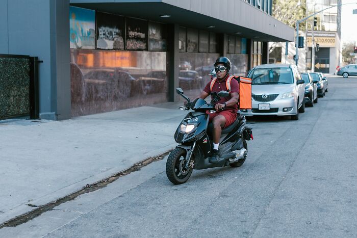 A delivery worker on a scooter with a large orange bag on his back, illustrating customer interactions.