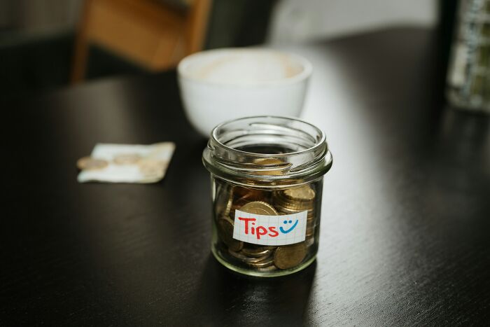 A glass jar filled with coins and a 'Tips' label, reflecting customer interactions and retail workers.