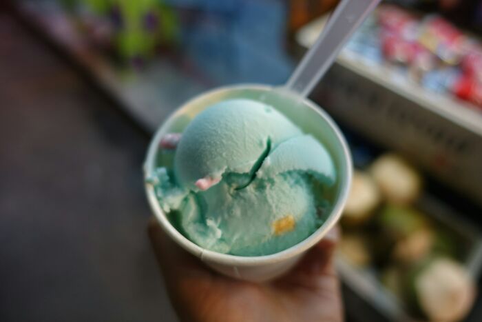 A hand holding a cup of light blue ice cream with sprinkles, representing customer interactions.