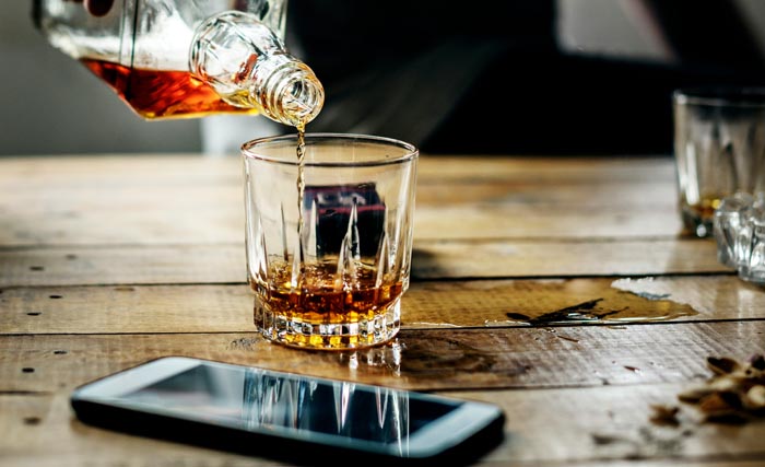 Whiskey being poured into a glass, next to a phone. A visual metaphor for an entitled parent's late reaction.