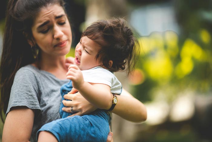 A nanny looking frustrated while holding a crying baby, illustrating an entitled parent's late arrival.