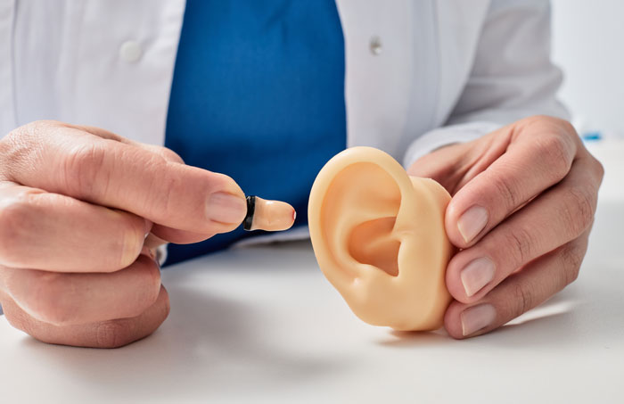 A medical worker holds a prosthetic ear and a small hearing aid, demonstrating the medical device. A medical worker holds a prosthetic ear and a small hearing aid, demonstrating the medical device.