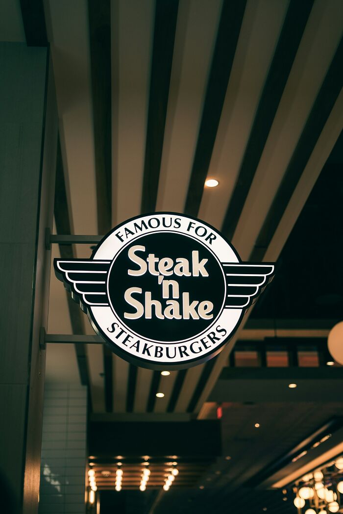Steak n Shake sign, famous for steakburgers, hanging indoors. Highlights a drive-through menu.