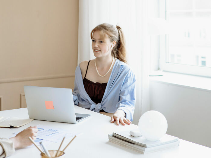A young coworker in casual attire, perhaps sharing spicy personal details with a colleague at her laptop.