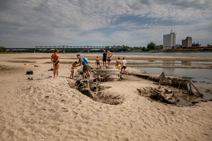 Europe suffers brutal drought: families explore exposed remnants of a ship on a dry riverbed, a sign of extreme drought.