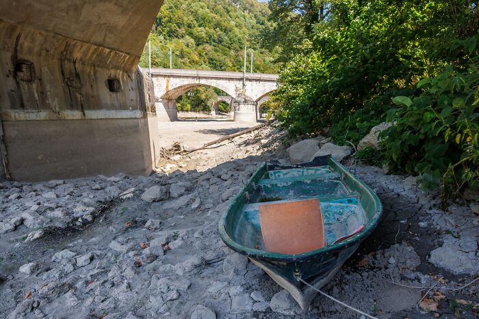 A small boat stranded on dry, cracked earth under a bridge, symbolizing the brutal drought affecting Europe.