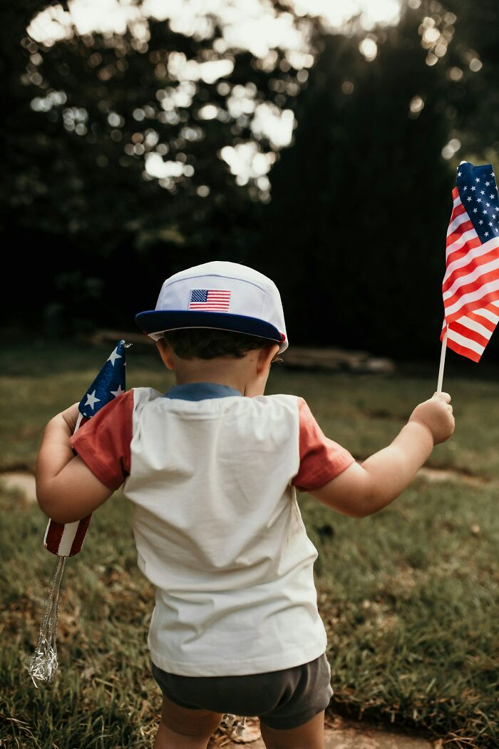 A young child holding American flags, symbolizing Americans who might ask Europeans interesting questions.