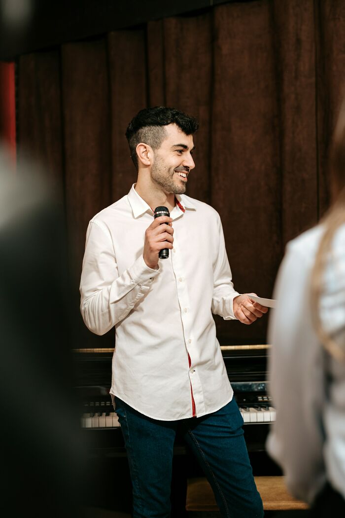 A man holding a microphone and smiling, possibly at an event where Americans asked Europeans questions.