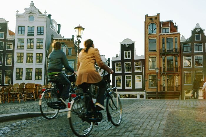 Two Europeans cycling past historic buildings in a European city, highlighting common questions Americans ask Europeans.