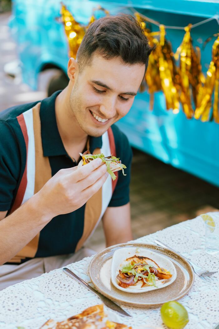 A man happily eating a taco at an outdoor table, representing the unique questions Americans asked Europeans.
