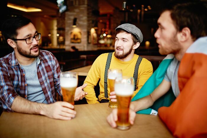 Three men in a pub, holding beers and conversing. Americans asked Europeans many questions that left them wondering.