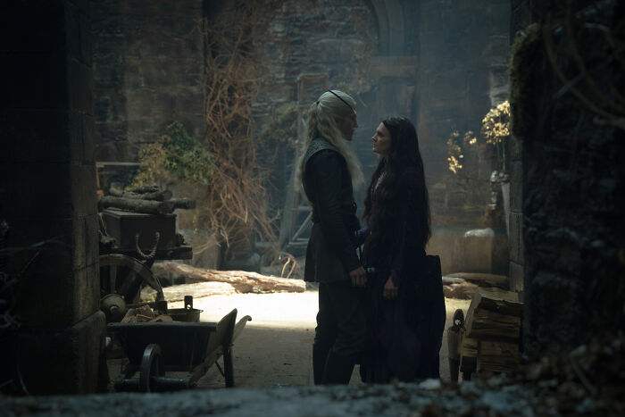 Two characters, one with long white hair and another with dark hair, standing face to face in an intimate scene from House of the Dragon. Two characters, one with long white hair and another with dark hair, standing face to face in an intimate scene from House of the Dragon.