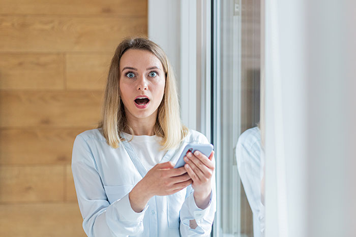 A woman with wide eyes holds a phone, expressing shock at her jobless ex-husband's attempt to take her home. A woman with wide eyes holds a phone, expressing shock at her jobless ex-husband's attempt to take her home.