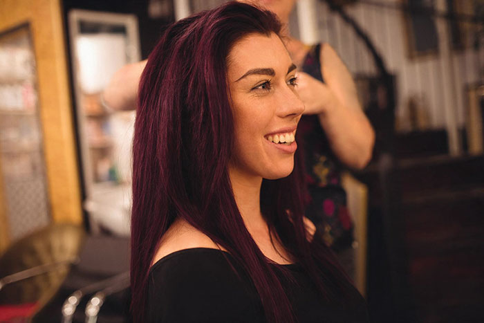 A woman with vibrant new hair color, smiling as a stylist works on her hair, after her boyfriend tried to ban her.