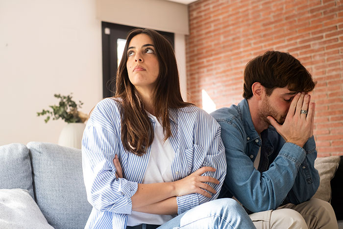 A woman with her arms crossed looks away from a man covering his face, showing a GF's hair color dispute.