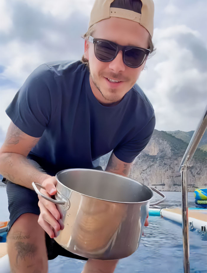 Brooklyn Beckham looking at the camera, holding a cooking pot while on a boat for his latest cooking video.