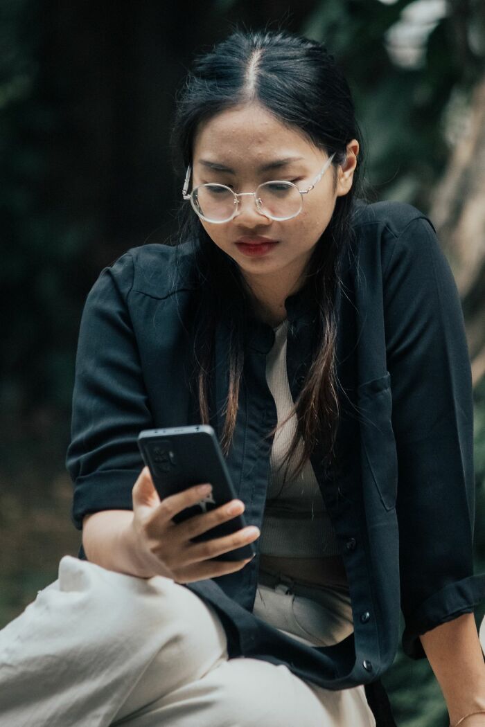A young woman with glasses looking at her phone, reflecting on people in her life she can't respect anymore.