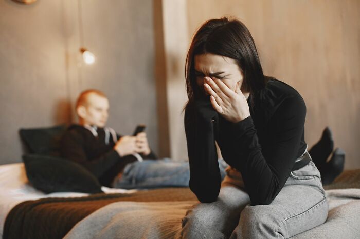 A woman cries on a bed while a man uses his phone, showing distress over people in their lives they can’t respect.