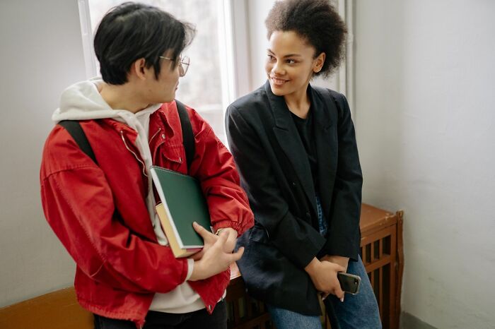 A young man with glasses and a red jacket talking to a smiling young woman. People in their lives.