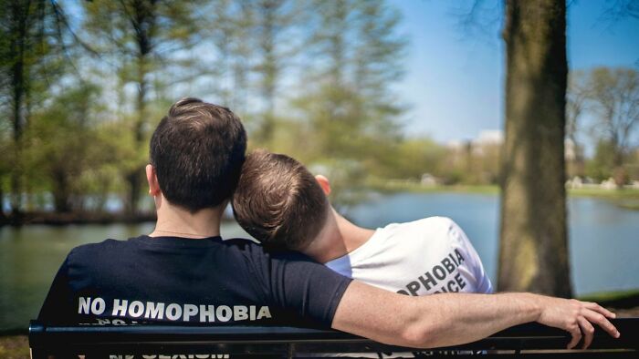 Two men sitting on a park bench, one with his head on the other's shoulder, discussing people they can't respect.
