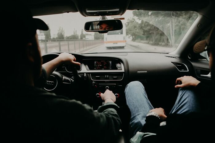 View from the back seat of a car showing two men in the front, driving. People in their lives.