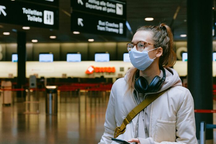 A woman in an airport wearing a face mask and headphones, pondering people in her life she can't respect anymore.