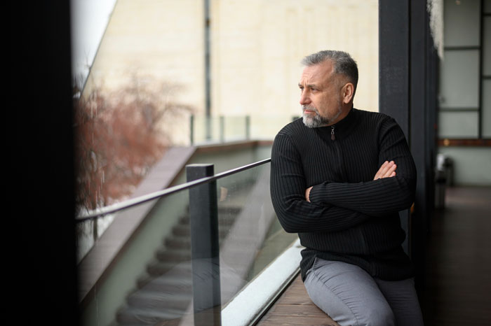 A thoughtful father looks out a window, reflecting on his strained father-daughter bond due to a paranoid mom. A thoughtful father looks out a window, reflecting on his strained father-daughter bond due to a paranoid mom.