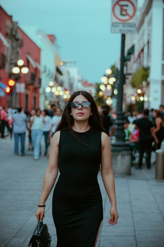Woman in a black dress and sunglasses walking on a city street. This image illustrates the savage ways women shut down creepy men.