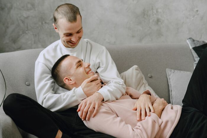 Two men smiling and cuddling on a grey couch. Women shut down creepy men with savage ways.
