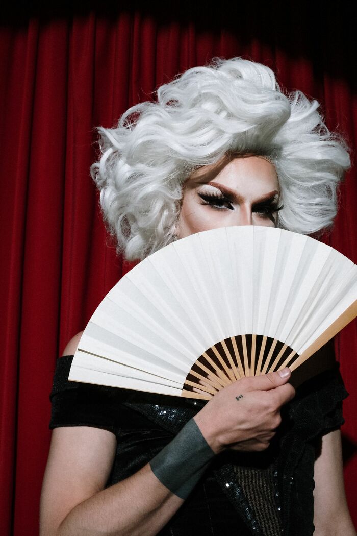 A person in a white wig and makeup holding a fan, depicting women shutting down creepy men.